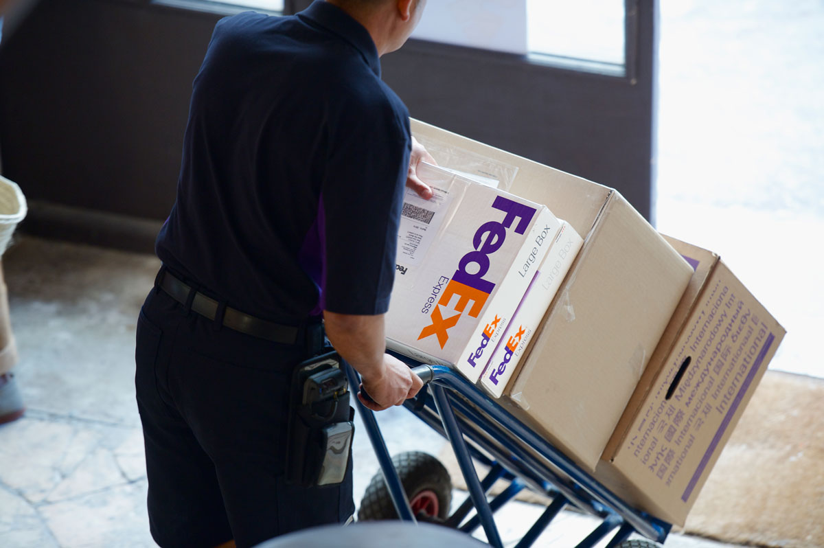 FedEx delivery driver wheeling a cart of boxes into a business